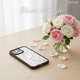 Phone case with floral design next to a vase of pink and white roses on a light surface.